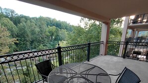 Ein Balkon mit einem runden Metalltisch und zwei Stühlen, mit Blick auf eine bewaldete Landschaft.