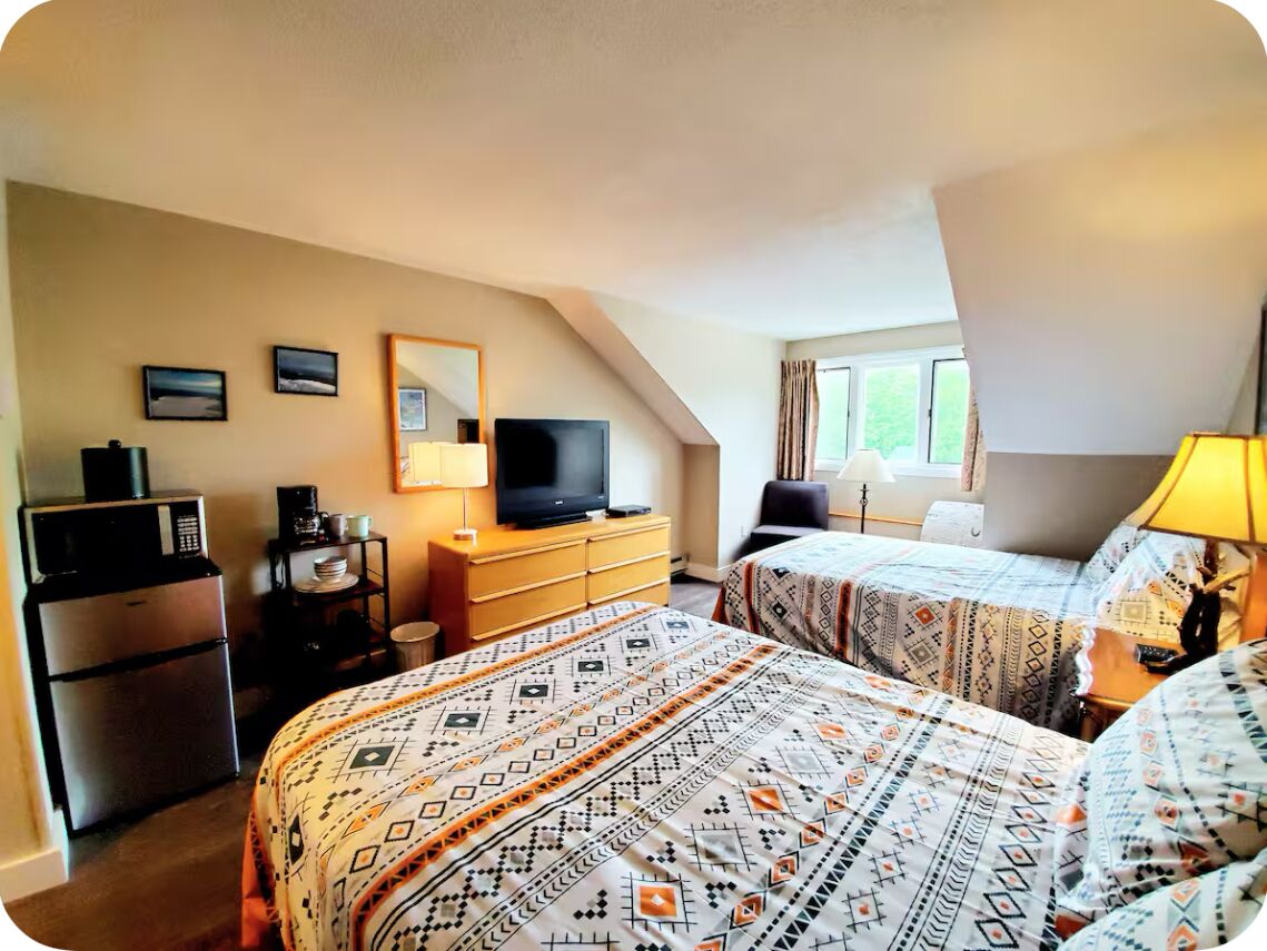 Une chambre d’hôtel avec deux lits, une télévision, un bureau avec un ordinateur, un réfrigérateur et une fenêtre avec des rideaux.