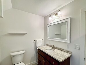 Un baño con inodoro, tocador con lavamanos y espejo.