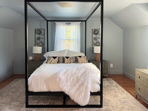 Un dormitorio con una cama con dosel, una mesita de noche con lámpara y un aparador.