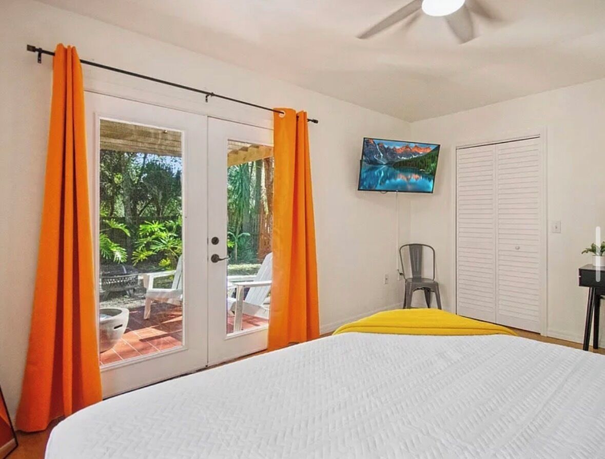 A bedroom with a bed, a ceiling fan, a TV, and a sliding door to a patio.