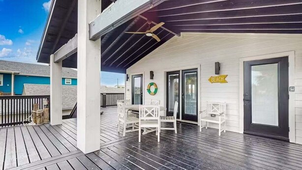 Un espace extérieur abrité, équipé d’une table et de chaises, d’un ventilateur de plafond et d’un panneau indiquant l’emplacement d’une plage.