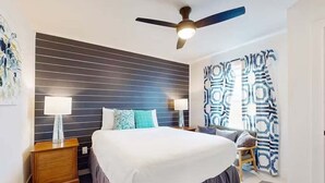 Une chambre moderne avec un grand lit, deux tables de chevet, un ventilateur de plafond et des rideaux à motifs.
