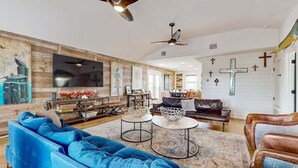 Un salon spacieux avec un canapé bleu, une table basse et une cheminée. On y trouve également des ventilateurs de plafond et un grand téléviseur fixé au mur.