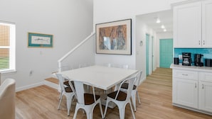 Een moderne keuken met witte kasten, een witte eettafel met stoelen en een koffiezetapparaat op het aanrecht.