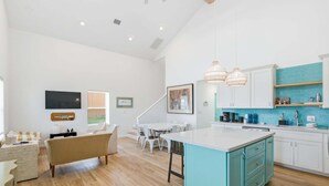 Een moderne keuken met witte kastjes, een turquoise eiland en hangende lampen.