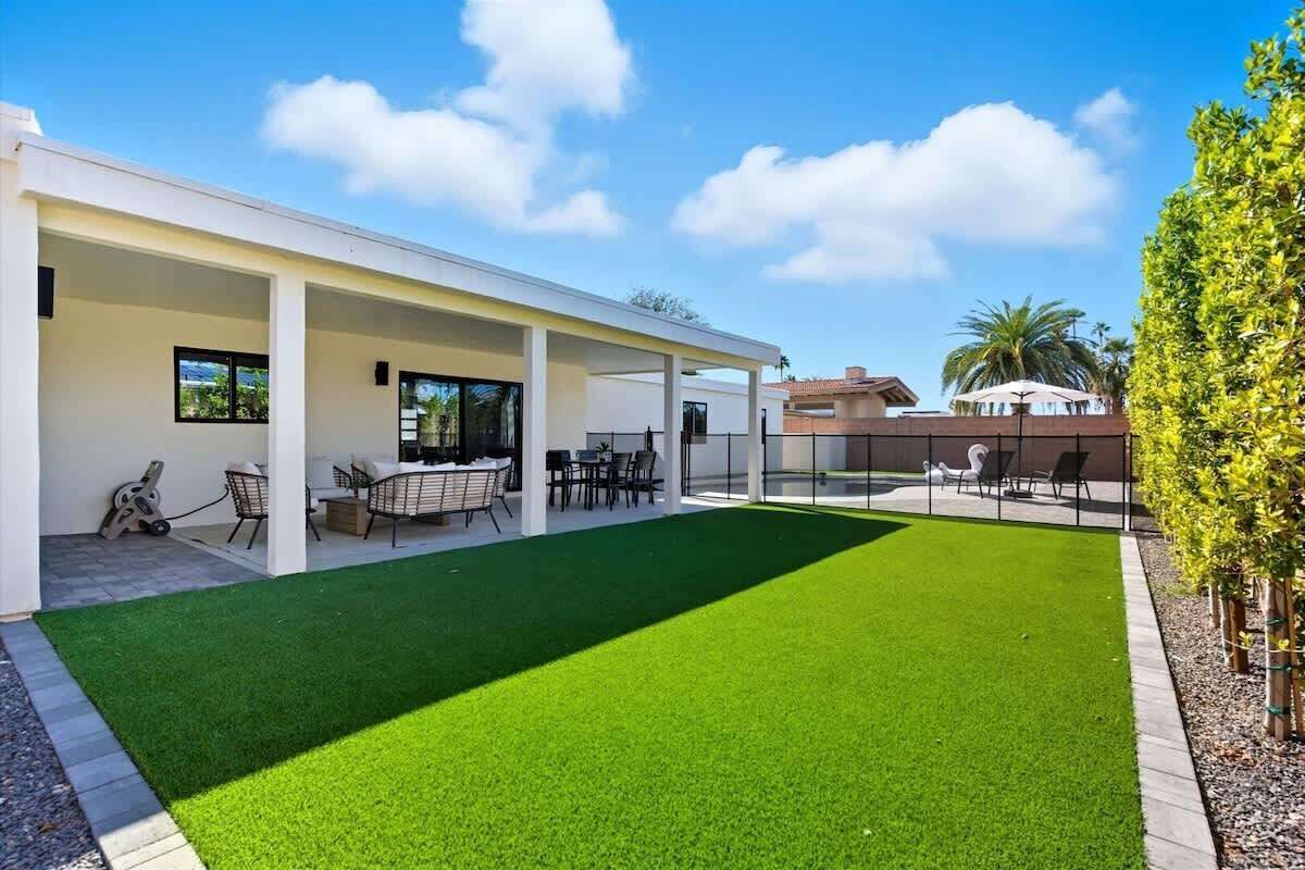Una casa moderna con patio cubierto, césped artificial verde y mobiliario exterior.