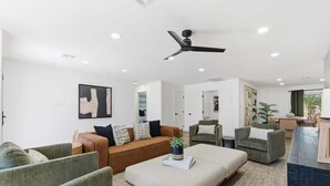 Uma sala de estar moderna com sofá, poltronas, mesa de centro e ventilador de teto.