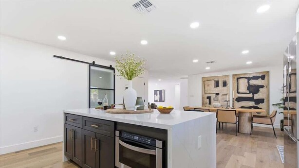 Uma cozinha moderna com ilha central, armários escuros e área de jantar com mesa e cadeiras.