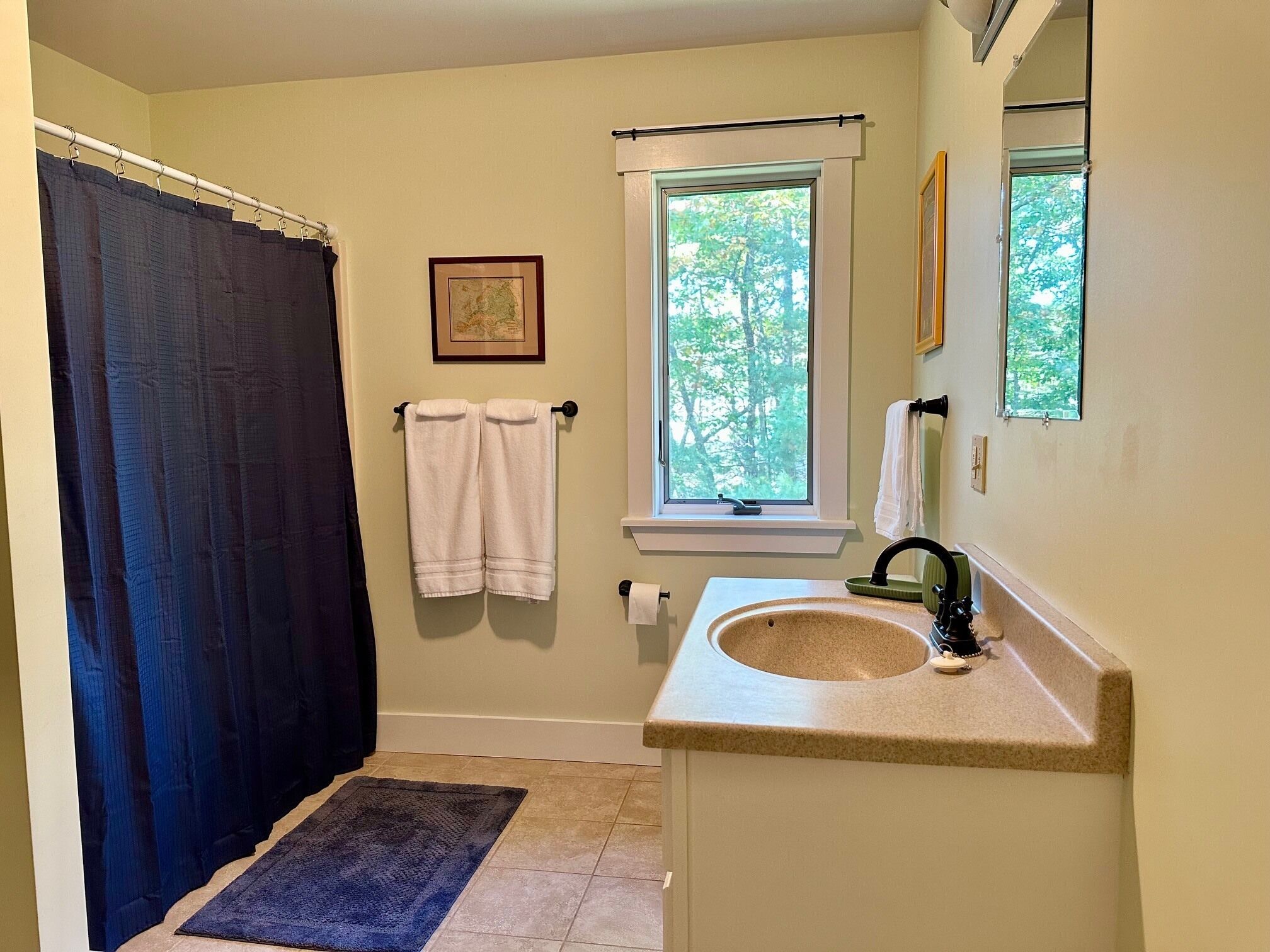 A bathroom with a shower curtain, a window, a sink, and a mirror.