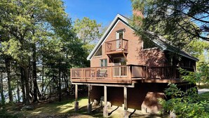 A two-story brick house with a balcony, surrounded by trees and a grassy area.