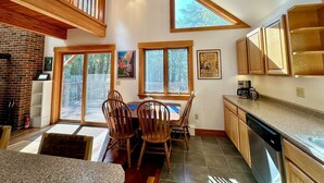 A spacious kitchen with wooden cabinets, a dining area with two wooden chairs, and large windows providing natural light.