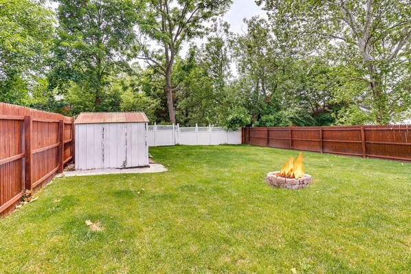 A backyard with a wooden fence, a shed, and a fire pit.