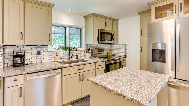 Una cocina moderna con armarios color beige, encimera de granito, electrodomésticos de acero inoxidable y una ventana con vistas a zonas verdes.
