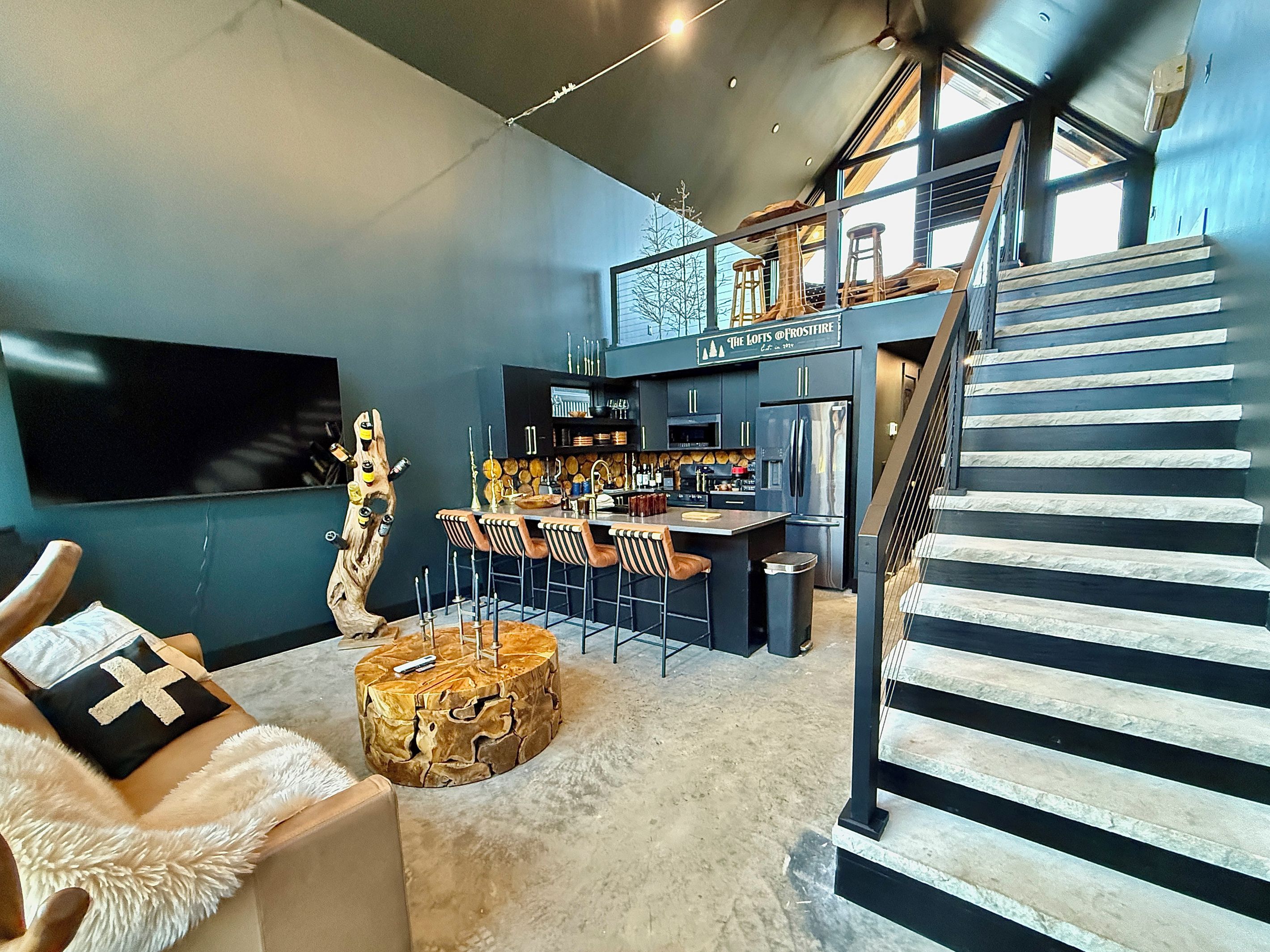 A modern kitchen with a bar area, a dining set, and a staircase leading to an upper level.