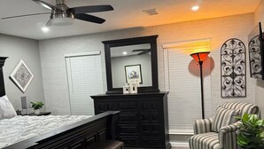 Um quarto com cama, cômoda, banco, cadeira e um tapete preto.