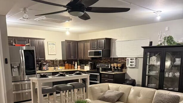 Uma sala de estar moderna com um sofá bege, uma mesa de centro de vidro e um ventilador de teto.