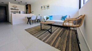 A modern living room with a sofa, a coffee table, and a dining area with chairs. - Makech Montebello - By Kanaa (Mérida)