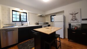 A compact kitchen with a wooden table, black bar stools, a dishwasher, a refrigerator, and a microwave. - Snowhawk House in Historic Wallace located close to many outdoor adventures! (Wallace)
