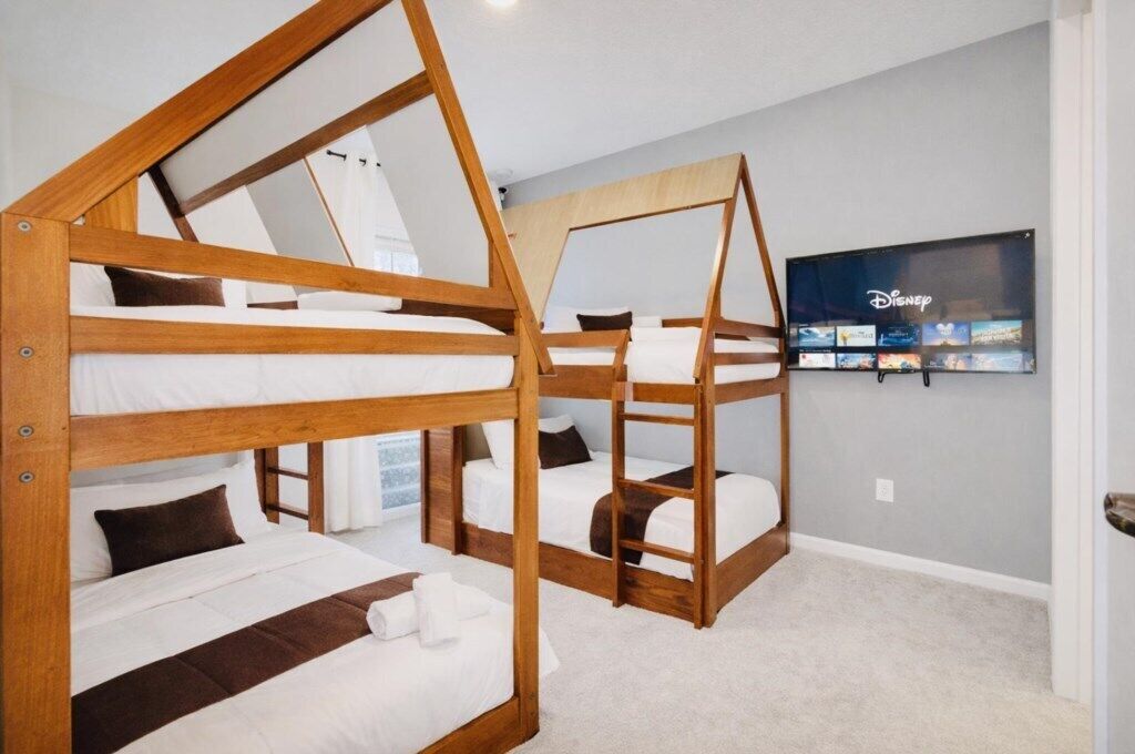 A room with bunk beds, a flat-screen TV mounted on the wall, and a carpeted floor.