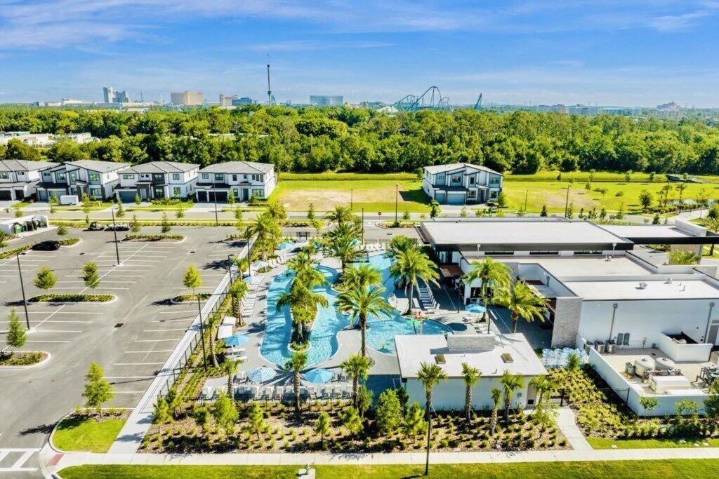 A modern hotel with a swimming pool, parking lot, and surrounding greenery.
