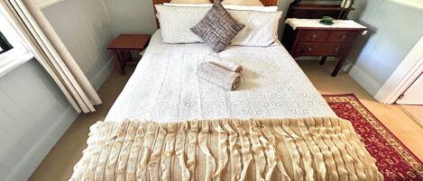 A neatly made bed with a patterned bedspread and pillows, a wooden headboard, a nightstand with a lamp, and a dresser with a mirror.