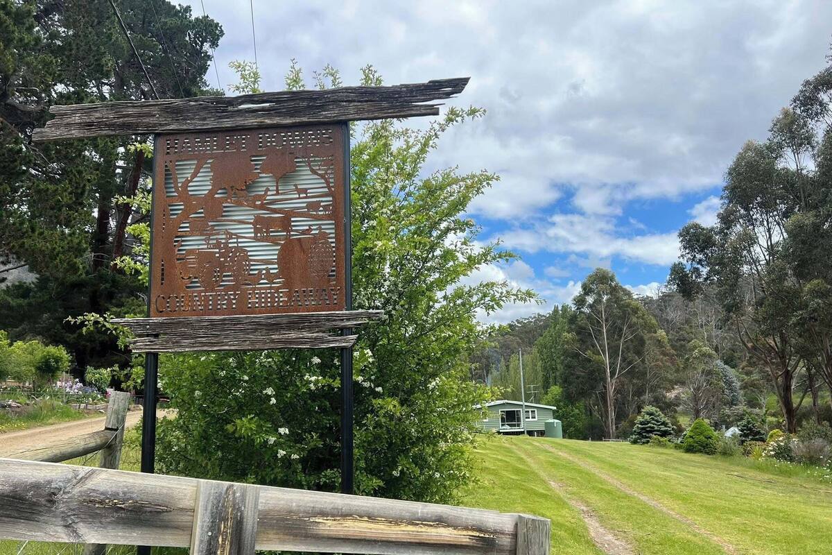 Un letrero metálico rústico con recortes de fauna silvestre, una cerca de madera y un edificio verde en un paisaje exuberante.