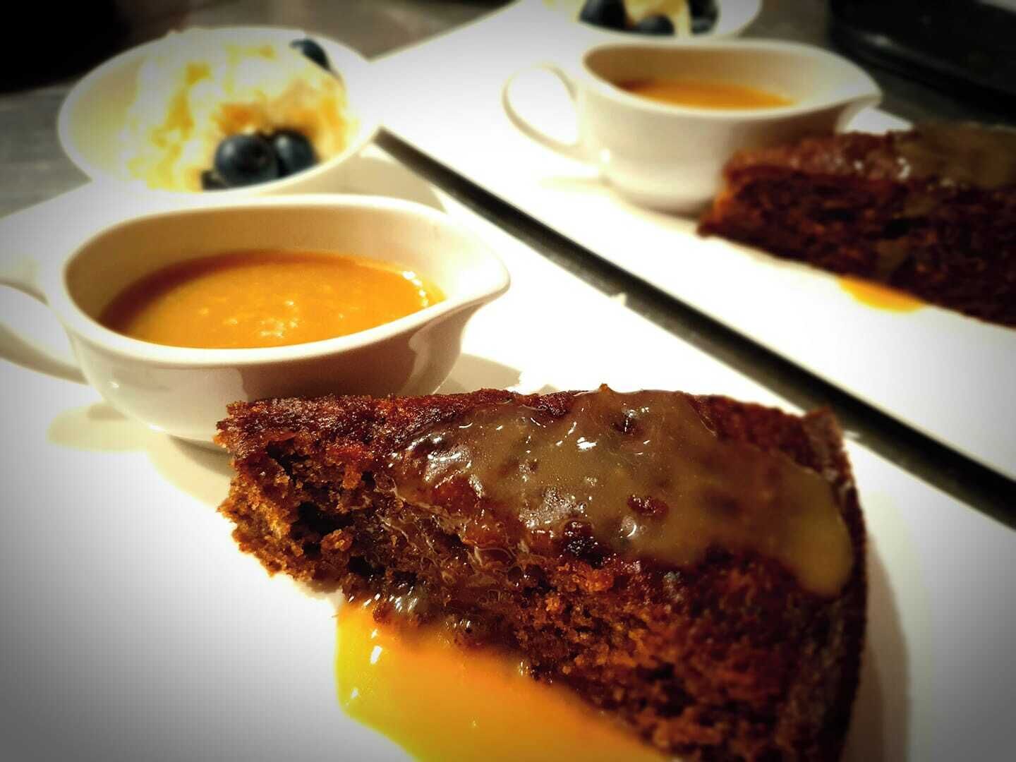 A dessert plate with a slice of cake topped with caramel sauce, accompanied by two bowls of soup.
