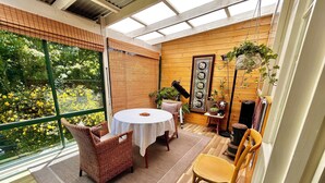 A sunlit room with a round table and wicker chairs, large windows, and wooden walls. - Hamlet Downs Country Accom (Fentonbury)