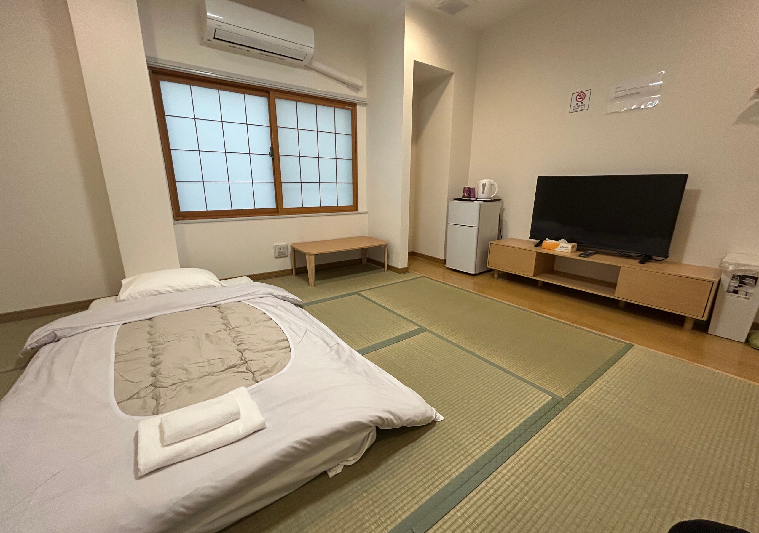 A hotel room with a bed, a television, a small table, a refrigerator, and a window with a view.