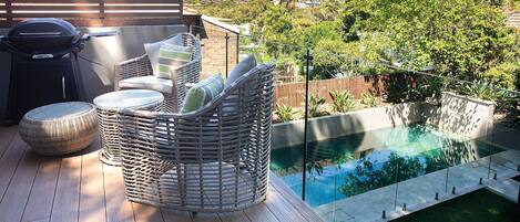 A patio with wicker furniture, a grill, and a swimming pool.