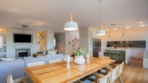 A modern kitchen with white cabinets, a wooden dining table, and pendant lighting. - Casa Piscina, Coogee Isyd (Coogee)