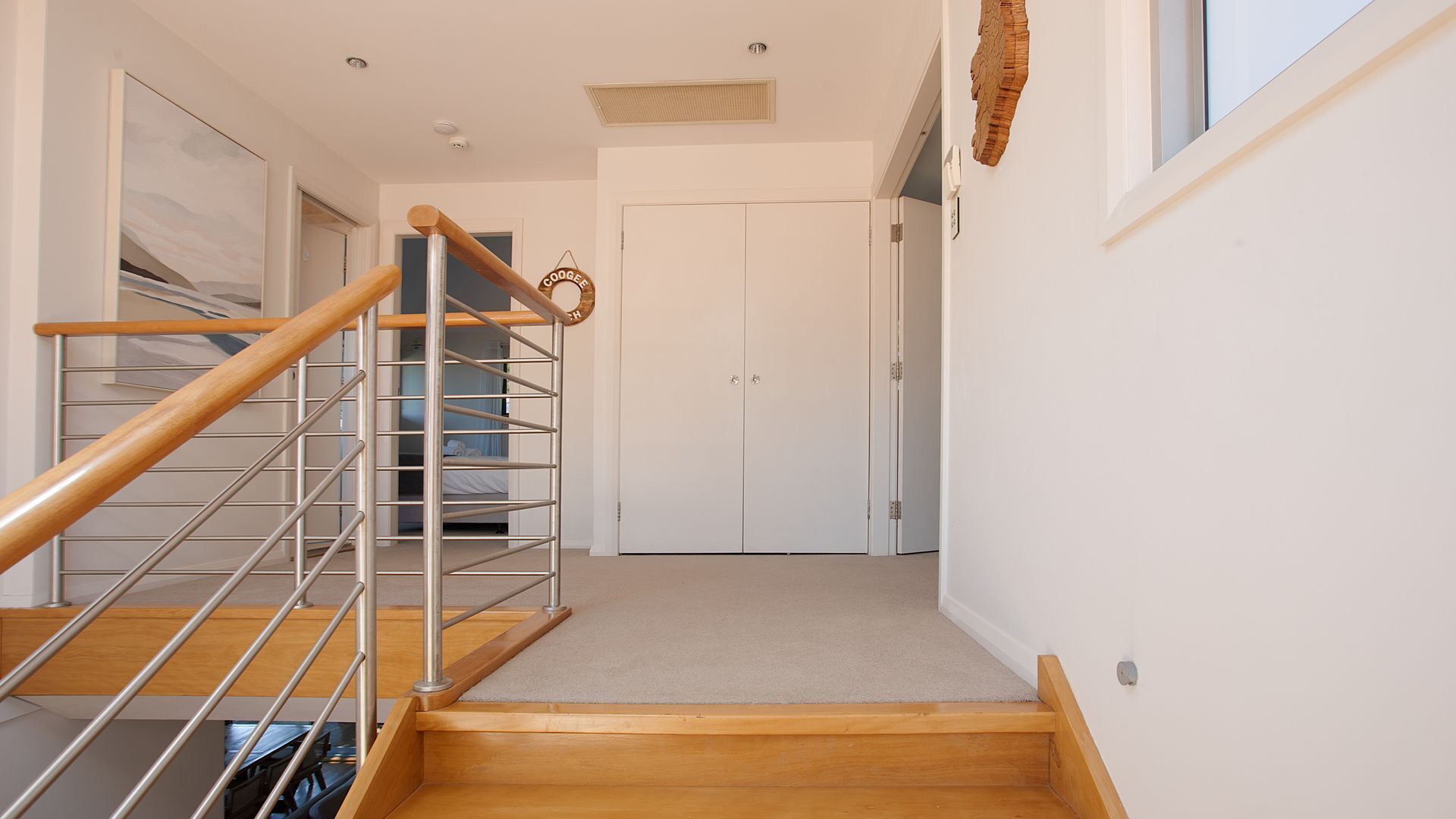 A staircase with a wooden handrail and metal balusters leading to a bedroom with a bed and a wardrobe.