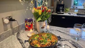 A kitchen counter with a pan of food, a vase of tulips, a candle, and a box of Cheetos.