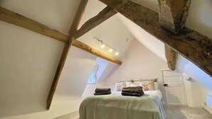 A bedroom with a sloped ceiling, exposed wooden beams, a bed with a green bedspread, and a small window.