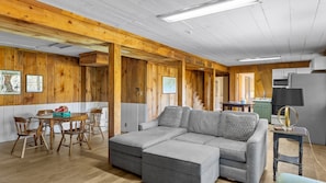 L’intérieur chaleureux d’un chalet comprend un coin repas en bois, un canapé d’angle gris et une cuisine équipée d’un réfrigérateur et d’un four à micro-ondes.