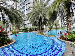A swimming pool with tiled blue mosaic flooring, surrounded by palm trees and a multi-story building in the background. - CELEDON Tân Phú (Ho Chi Minh City)