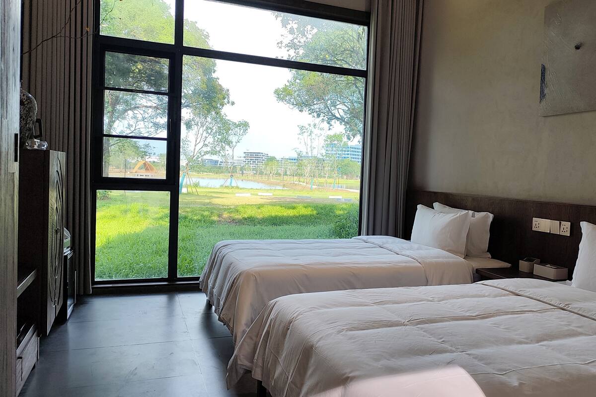 A hotel room with two beds, a large window, and a view of a park.