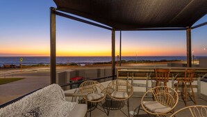 A covered outdoor seating area with wicker chairs and a table, overlooking a sunset over the ocean. - Trigg Coastal House - Beachfront Bliss with Sunset Views (Trigg)