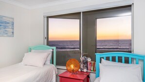 A bedroom with two beds, a nightstand with a lamp, and a view of the ocean at sunset. - Trigg Coastal House - Beachfront Bliss with Sunset Views (Trigg)