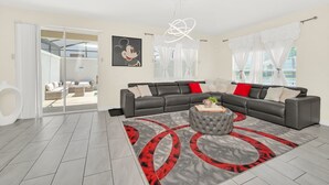 Ein modernes Wohnzimmer mit einem Ecksofa, einem runden Hocker und einem roten und grauen Teppich mit Muster.