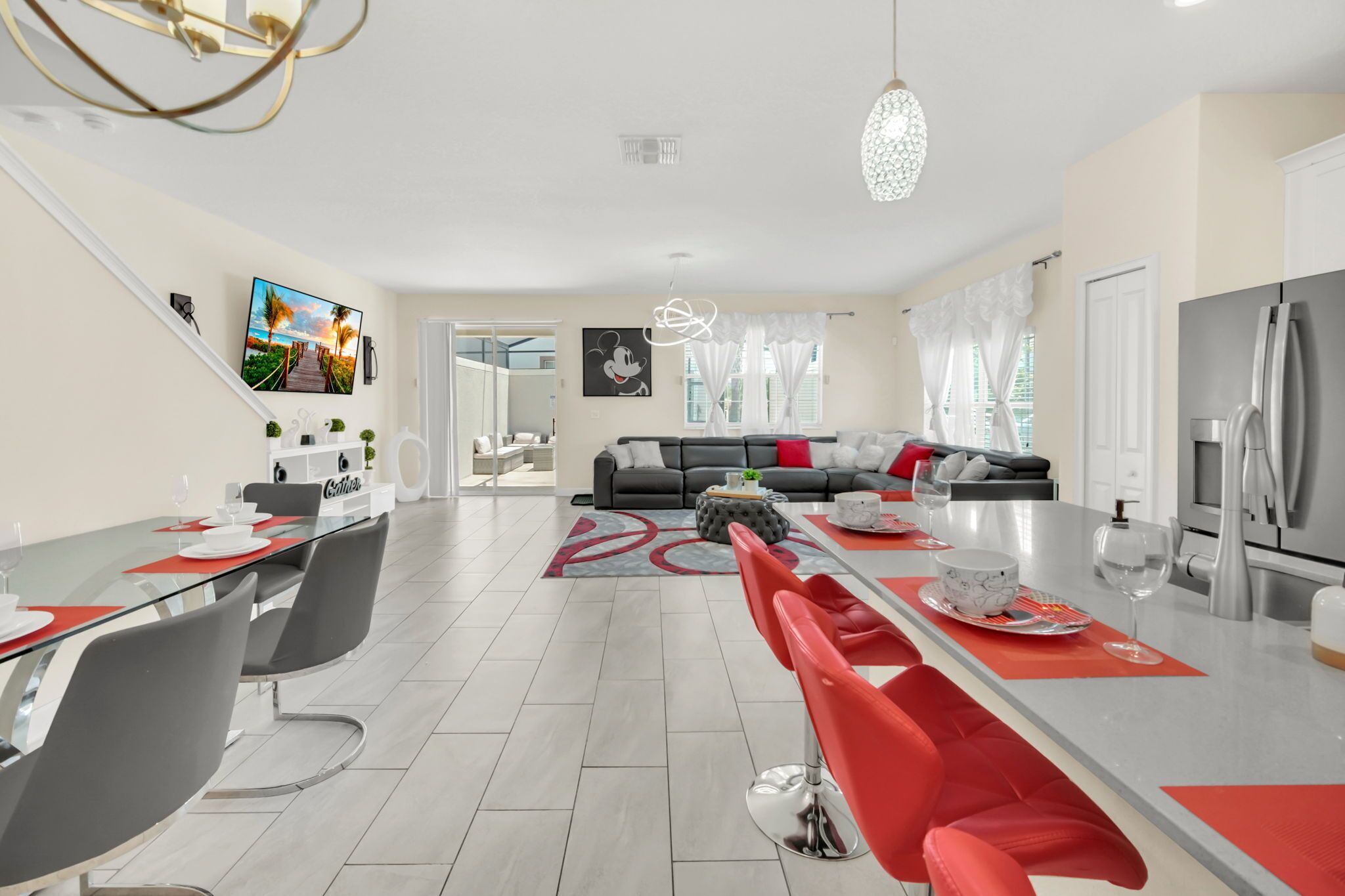 A modern kitchen with a central island, dining area with red chairs, and a living area with a sofa and TV.