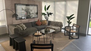 A modern living room with a grey sofa, a coffee table, and a chair. There are two side tables and a floor lamp. A large window provides natural light. - Nuñoa... one step away from everything you need (apartment 1105) (Ñuñoa)