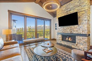 A modern living room with a stone fireplace, large windows, and a cozy seating area. - Moonlight Basin Retreat | Ski-In/Out + Patio (Big Sky)