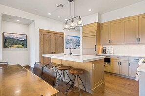 A modern kitchen with a large island, wooden cabinets, and bar stools. - Moonlight Basin Retreat | Ski-In/Out + Patio (Big Sky)