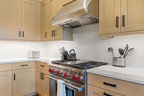 A modern kitchen with wooden cabinets, a stainless steel stove, and a toaster on the countertop. - Moonlight Basin Retreat | Ski-In/Out + Patio (Big Sky)