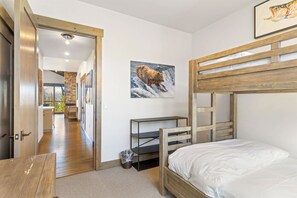 A bunk bed room with a wooden headboard, a small desk, and a picture of a bear on the wall. - Moonlight Basin Retreat | Ski-In/Out + Patio (Big Sky)