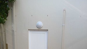 A white door with a vent, a blue mat, and a brown pot on a brick-paved area.