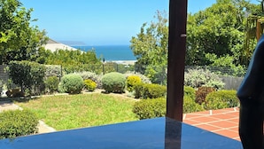 A clear view of the ocean from a glass table with a book and a bowl of food.