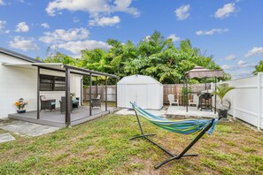 Een achtertuin met een overdekte patio, een hangmat en een omheind terras met tuinmeubilair.